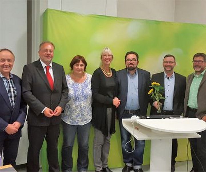 Gruppenfoto mit festlich angezogenen Personen vor einem grünen Aufsteller
