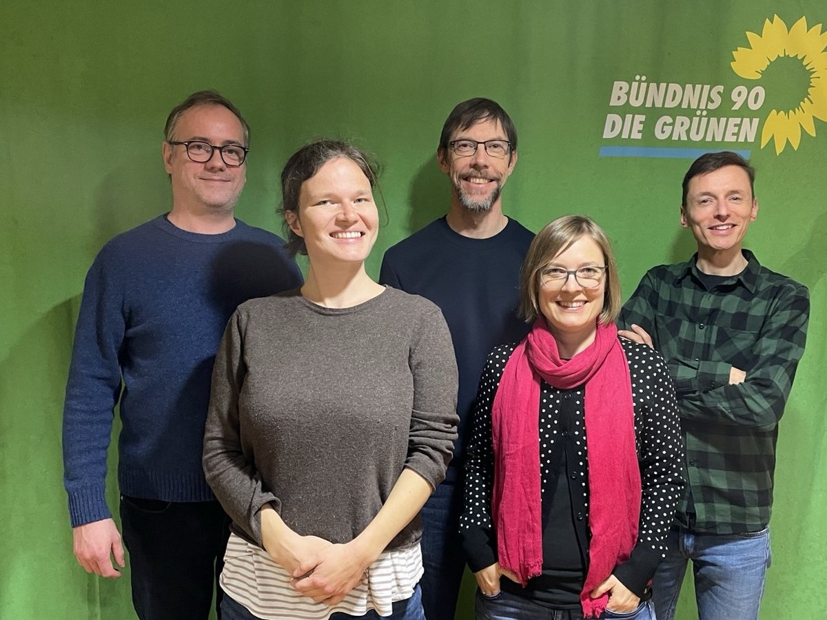 Gruppenfoto von den fünf Vorständ*innen vor einer grünen Wand mit dem Logo der Grünen
