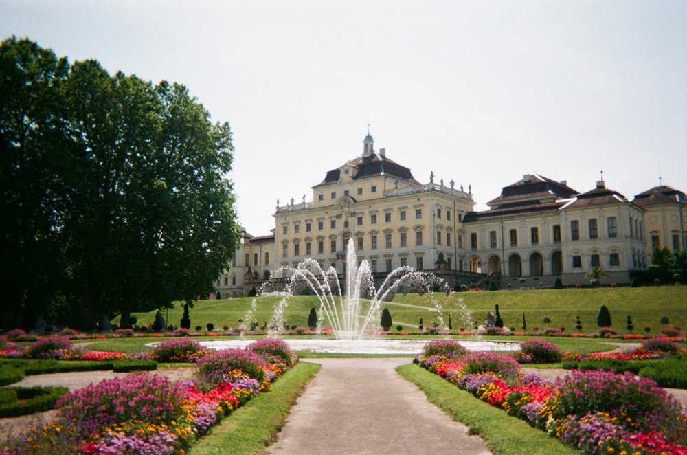 Das Ludwigsburger Schloss durch den Schlosspark hindurch fotografiert, in der Mitte des Bildes ist ein Springbrunnen.