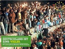 Foto vom Mauerfall. Viele Menschen stehen und sitzen auf der Mauer, viele halten Wunderkerzen in der Hand. Aufschrift: Deutschland ist Eins: Vieles.
