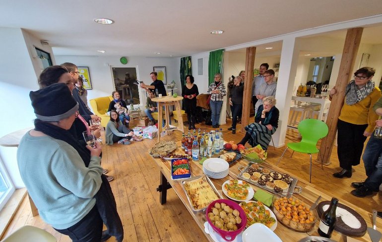 Bild von einem Stehempfang, in der Mitte ist ein Buffet.