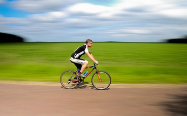 Foto von einem Mann in Sportkleidung, der auf einem Rennrad über eine Landstraße fährt.